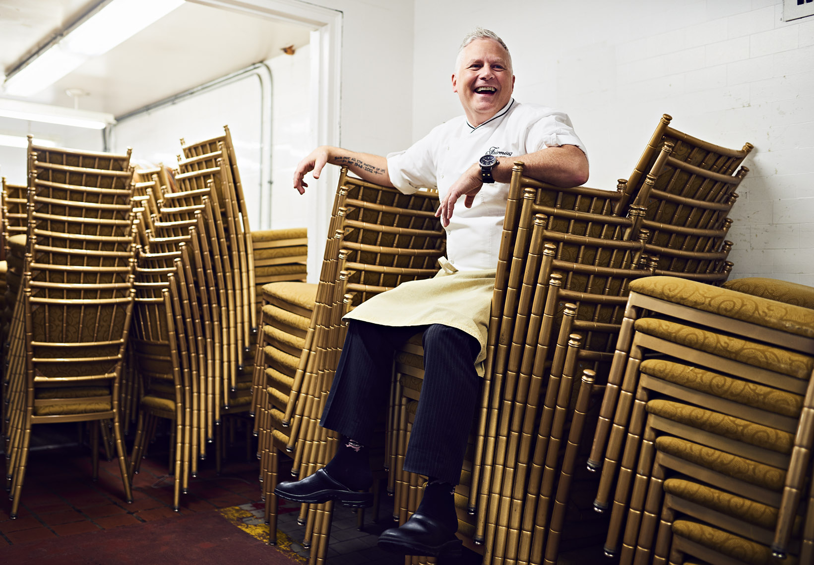 Laughing chef sitting on piled chairs and looking off