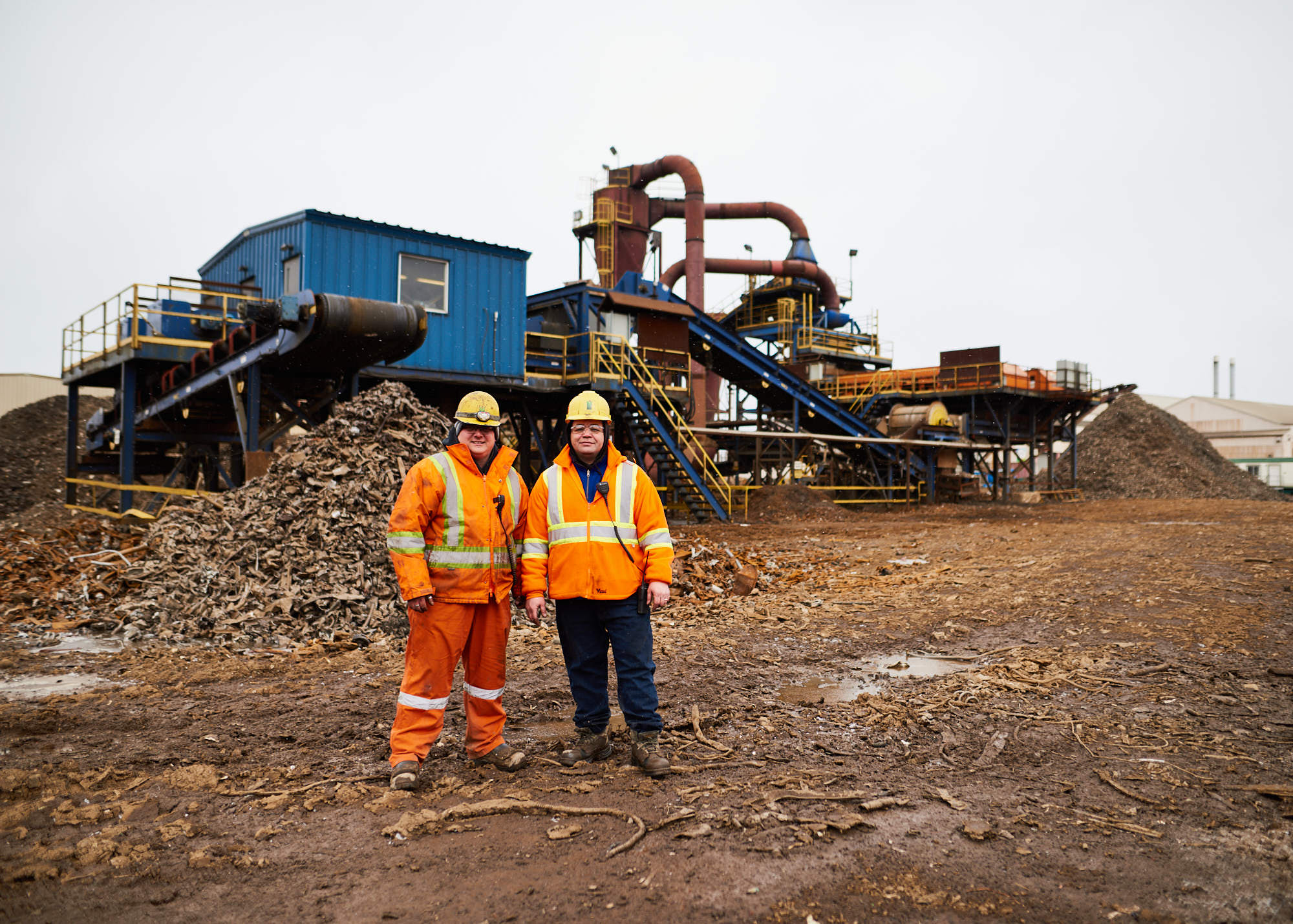 Industrial photography portrait of two male steel workers standing outside manufacturing and recycling machinery